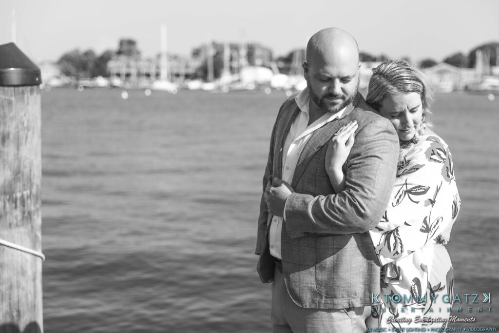 A couple standing by the water, with the woman leaning on the man's shoulder.