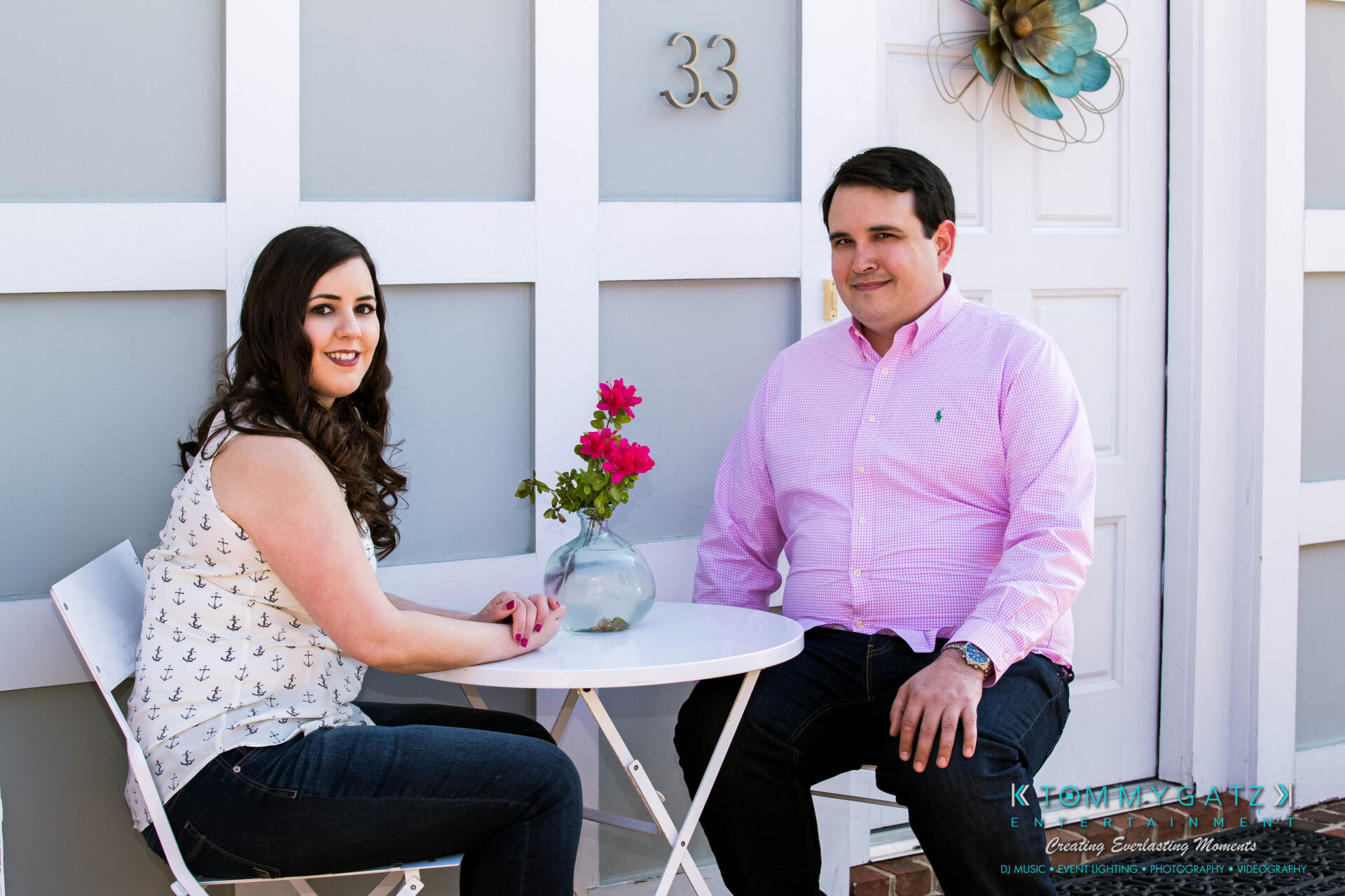 JamieMark-Engagement-20 - TOMMY GATZ ENTERTAINMENT A man and woman sitting at a small outdoor table with a vase of flowers.