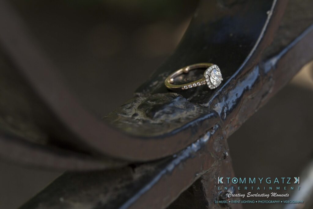 Jennifer-Rudi-Engagement-6102017-Blog-WM-11 - TOMMY GATZ ENTERTAINMENT A diamond engagement ring rests on a curved metal surface.