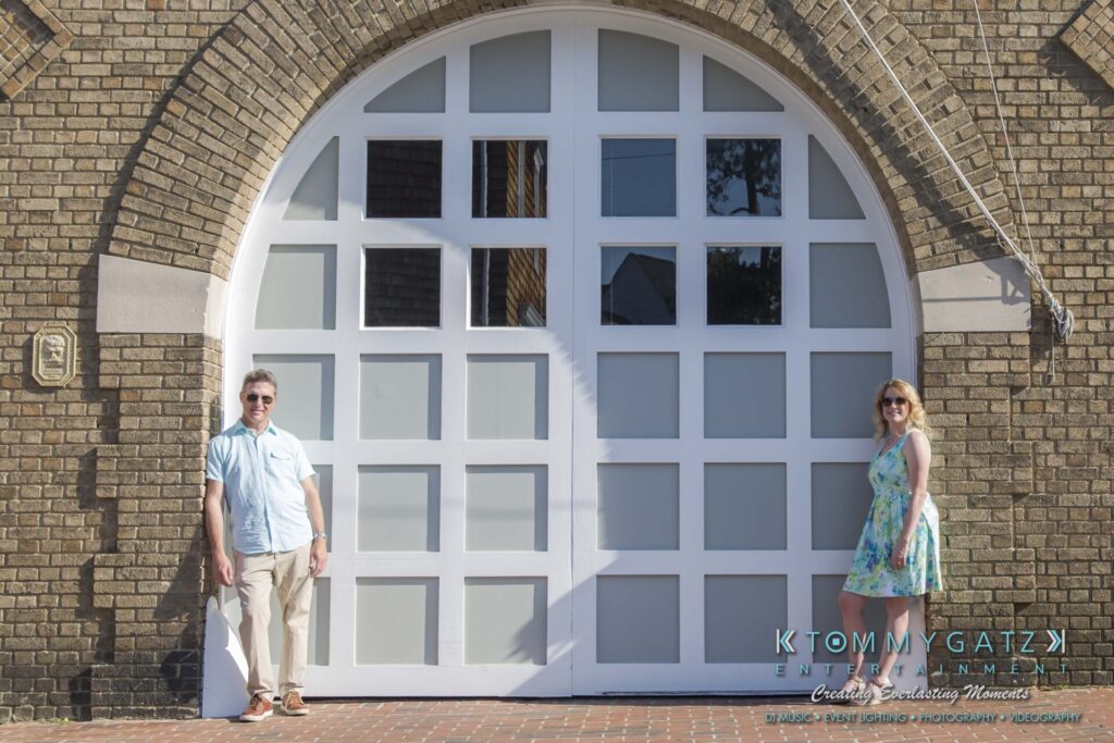 Jennifer-Rudi-Engagement-6102017-Blog-WM-44 - TOMMY GATZ ENTERTAINMENT A man and woman stand apart in front of a large, arched doorway with white grid windows.