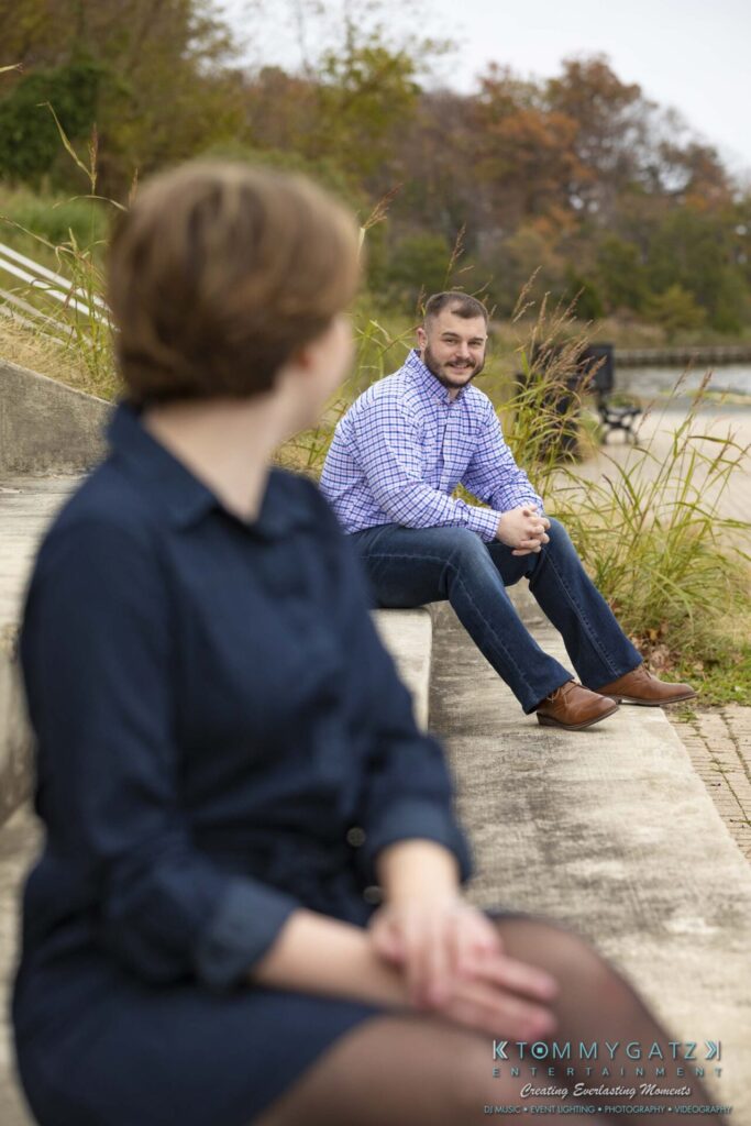 Jon-Christine-111218-Blog-Low-Res-27 - TOMMY GATZ ENTERTAINMENT A person in a blue dress is sitting on steps in the foreground, facing away. In the background, a person in a checked shirt is sitting on steps, facing forward. Grass and trees are nearby.