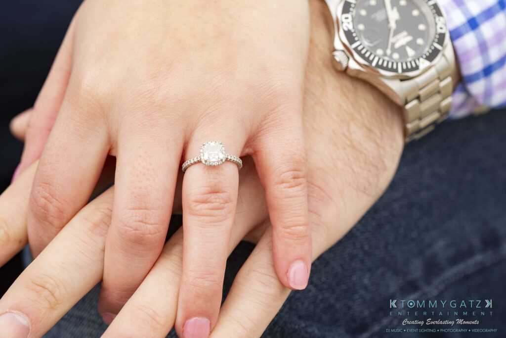 Jon-Christine-111218-Blog-Low-Res-9 - TOMMY GATZ ENTERTAINMENT Close-up of a diamond engagement ring on a person's hand, resting atop another hand wearing a wristwatch.
