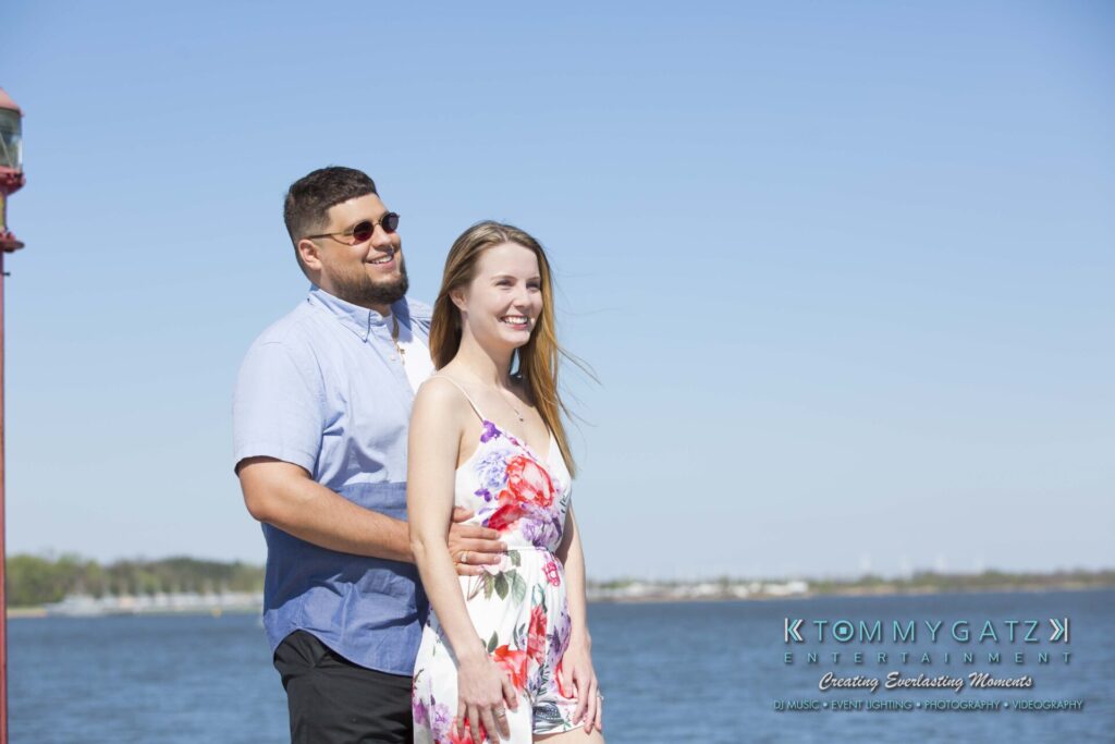 Kari-Jose-43018-FINALS-Low-Res-WM-13 - TOMMY GATZ ENTERTAINMENT A man and a woman stand together smiling by a waterfront, with a clear blue sky in the background.