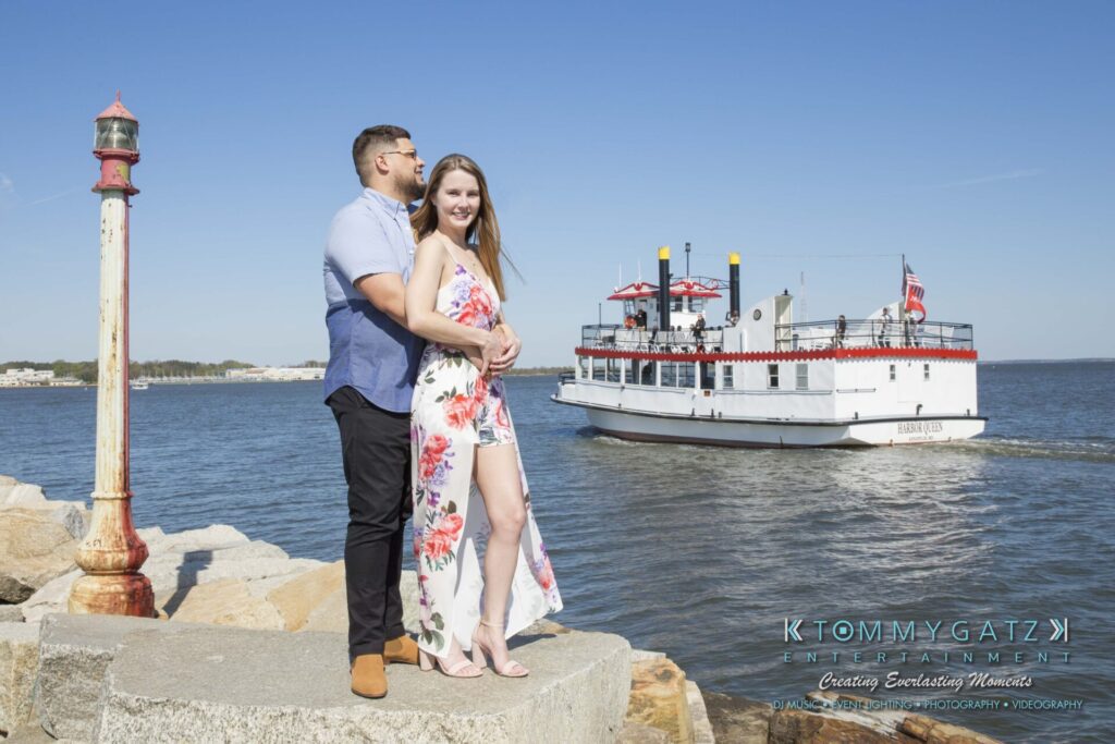 Kari-Jose-43018-FINALS-Low-Res-WM-15 - TOMMY GATZ ENTERTAINMENT A couple embraces on a stone ledge by the water, with a white ferry boat in the background and a lighthouse to the left.