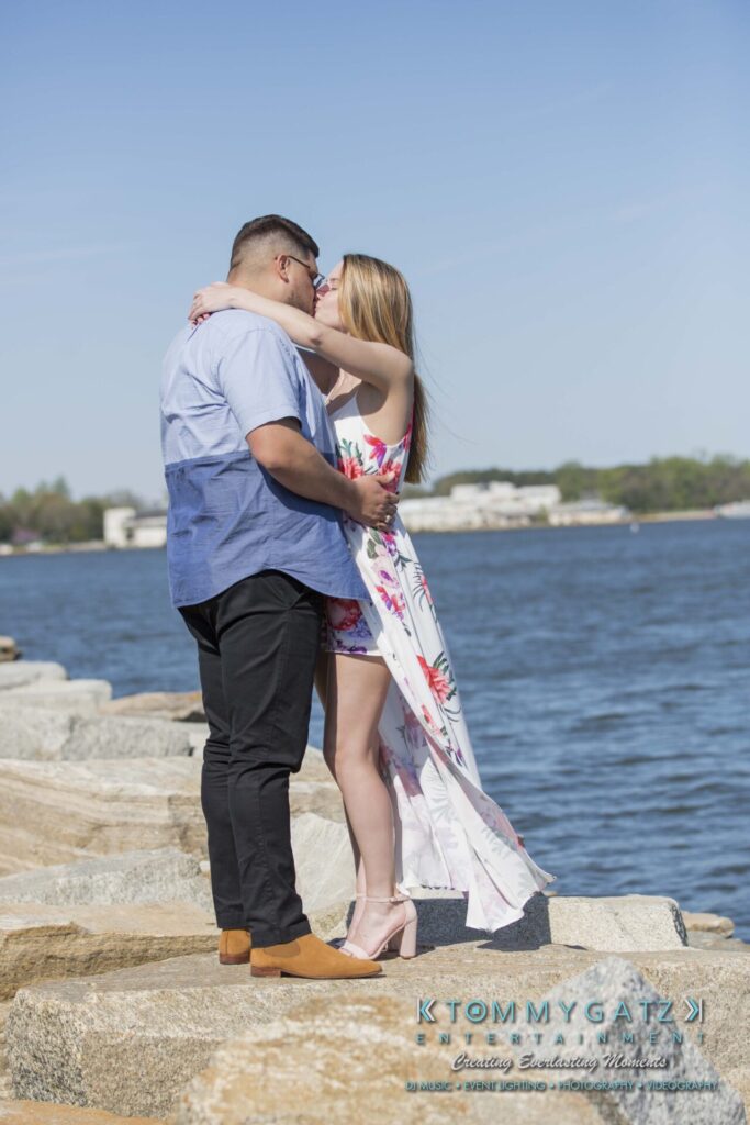 Kari-Jose-43018-FINALS-Low-Res-WM-20 - TOMMY GATZ ENTERTAINMENT A couple embraces on a rocky shore with water and distant buildings in the background.