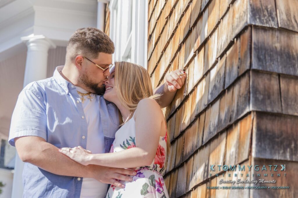 Kari-Jose-43018-FINALS-Low-Res-WM-36 - TOMMY GATZ ENTERTAINMENT A couple embraces and smiles against a shingle wall on a sunny day.