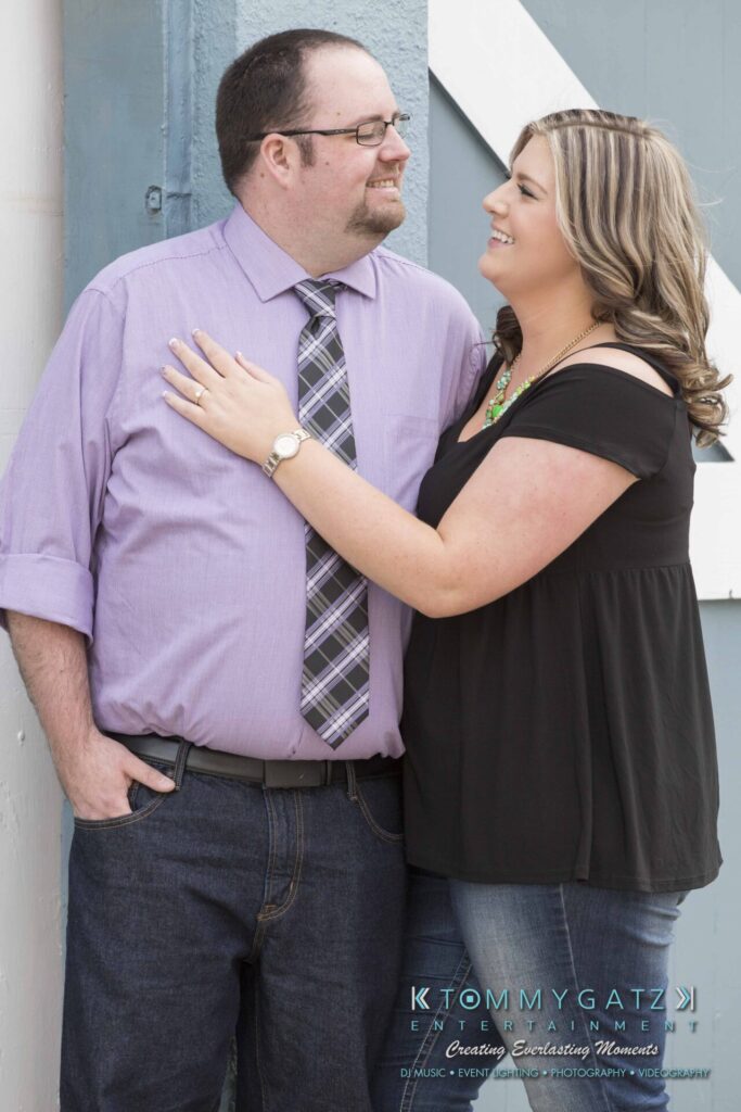 Lisa-Robert-Engagement-042218-Low-Res-Watermark-11 - TOMMY GATZ ENTERTAINMENT A man and woman stand closely, smiling at each other. The woman has her hand on the man's chest. Both are casually dressed.