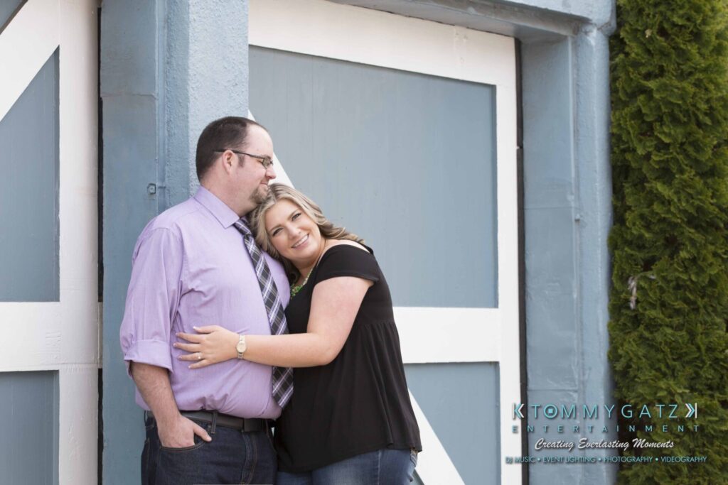 Lisa-Robert-Engagement-042218-Low-Res-Watermark-13 - TOMMY GATZ ENTERTAINMENT A couple stands in front of a blue and white door. The woman leans her head on the man's shoulder, and both are smiling.