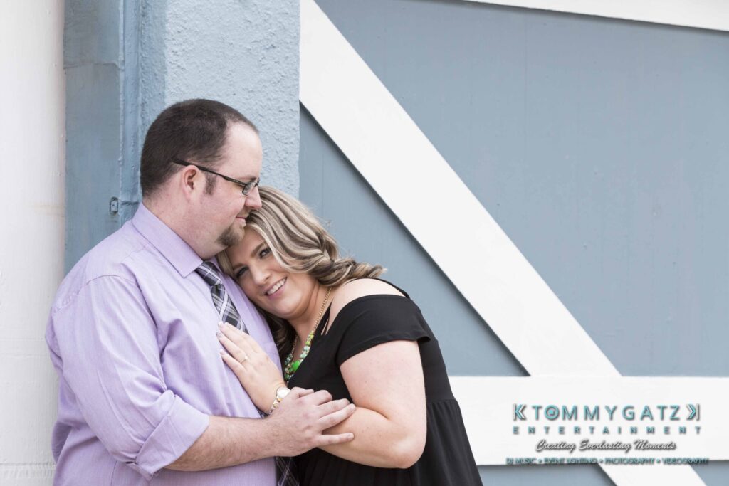 Lisa-Robert-Engagement-042218-Low-Res-Watermark-14 - TOMMY GATZ ENTERTAINMENT A smiling couple embraces in front of a large blue and white door. The man is in a purple shirt and the woman is in a black top.