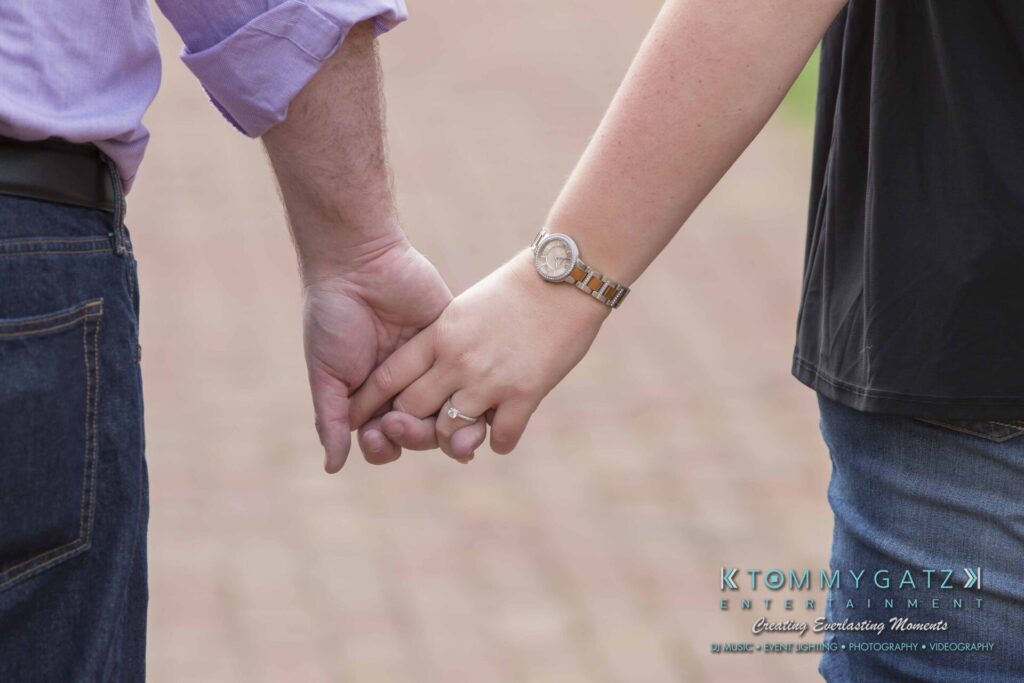 Lisa-Robert-Engagement-042218-Low-Res-Watermark-21 - TOMMY GATZ ENTERTAINMENT A couple holding hands, focusing on their wrists and joined hands, with a watch and ring visible.