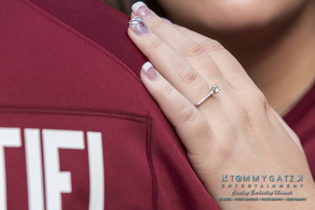 Lisa-Robert-Engagement-042218-Low-Res-Watermark-57 - TOMMY GATZ ENTERTAINMENT A person with a diamond ring on their finger rests their hand on another person's shoulder, visible in a maroon shirt.