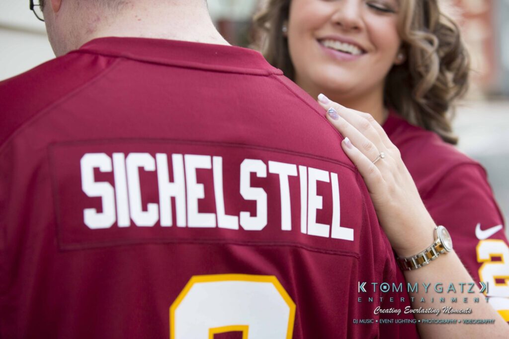 Lisa-Robert-Engagement-042218-Low-Res-Watermark-62 - TOMMY GATZ ENTERTAINMENT A person in a red sports jersey with the name "Sichelstiel" on the back. Another person smiles and touches their shoulder.