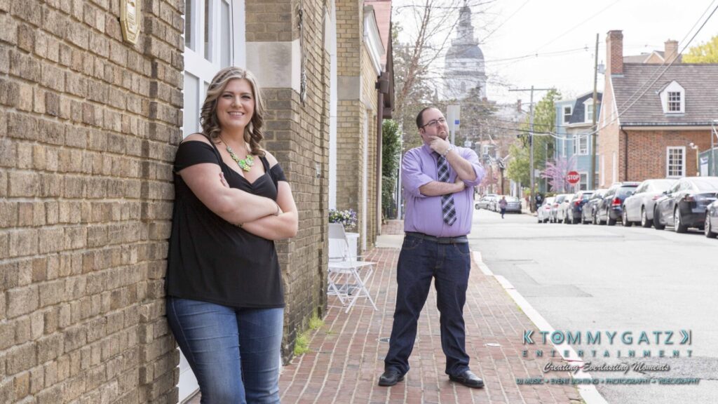 Lisa-Robert-Engagement-042218-Low-Res-Watermark-8 - TOMMY GATZ ENTERTAINMENT Two people standing on a sidewalk near brick buildings on a sunny day. The Capitol dome is visible in the background.