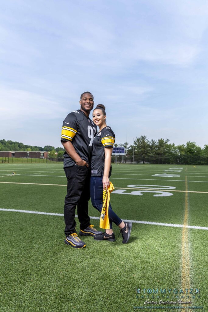051919-Viona-Kevin-FINALS-Low-RES-WM-31 - TOMMY GATZ ENTERTAINMENT Two people are standing on a football field wearing matching jerseys. The person on the right is holding a yellow towel.