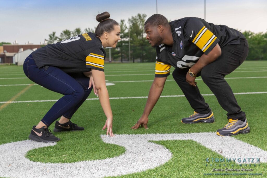 051919-Viona-Kevin-FINALS-Low-RES-WM-39 - TOMMY GATZ ENTERTAINMENT Two people in matching jerseys face each other in a squat position on a football field, near the number 50.