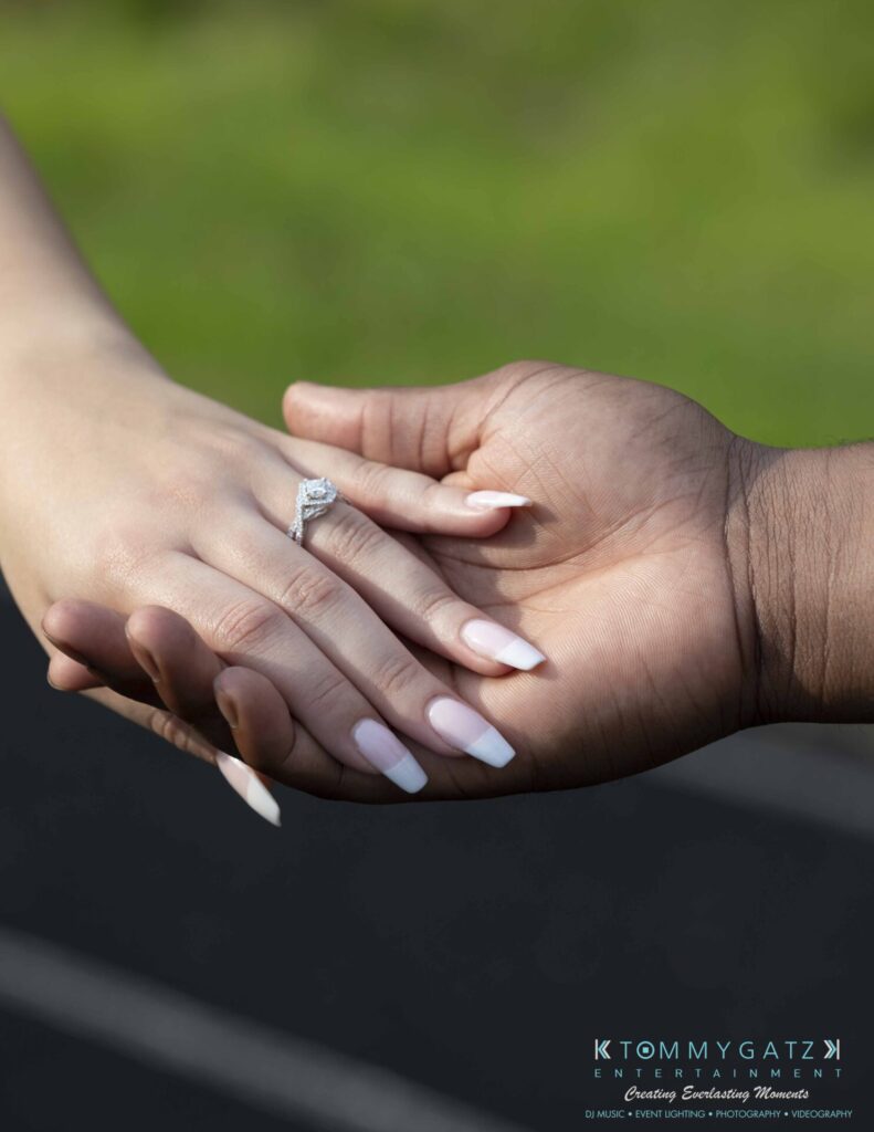 051919-Viona-Kevin-FINALS-Low-RES-WM-5 - TOMMY GATZ ENTERTAINMENT Close-up of two hands gently holding one another, with a diamond ring on the woman's finger. The background is blurred.