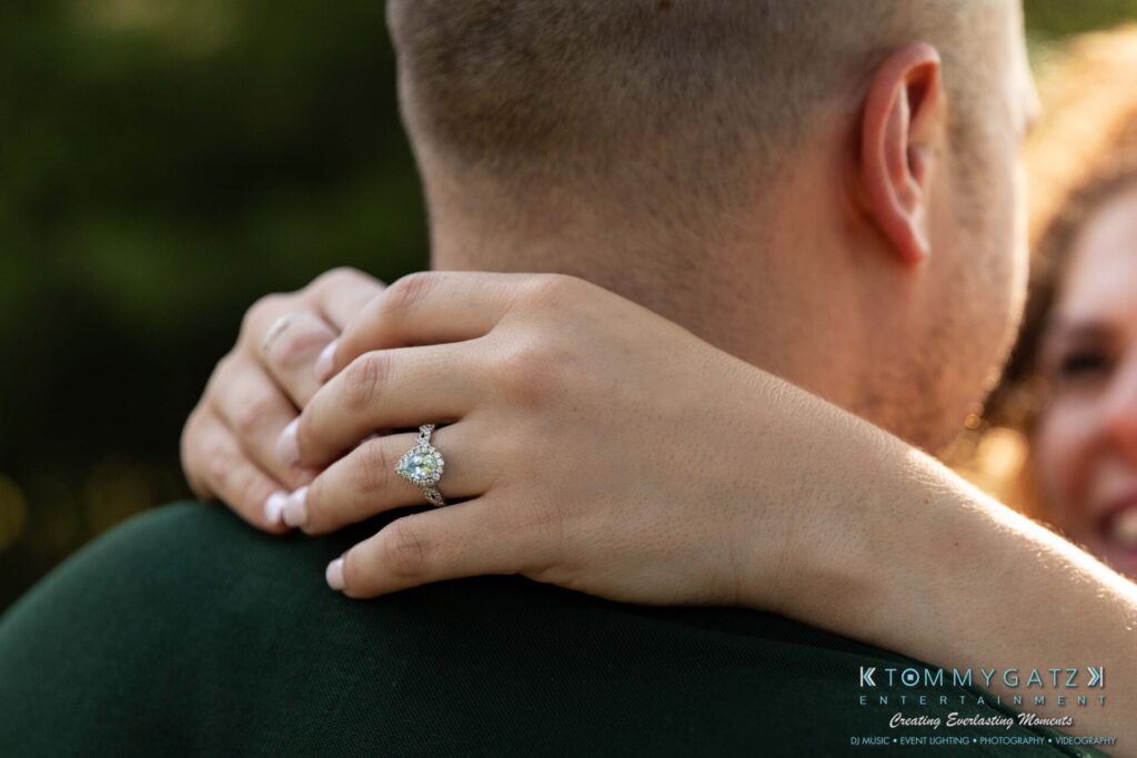 063019-Melanie-Rob-FINALS-Low-Res-WM-14 - TOMMY GATZ ENTERTAINMENT Close-up of a couple embracing, focusing on a woman's hand resting on the man's shoulder, displaying an engagement ring.