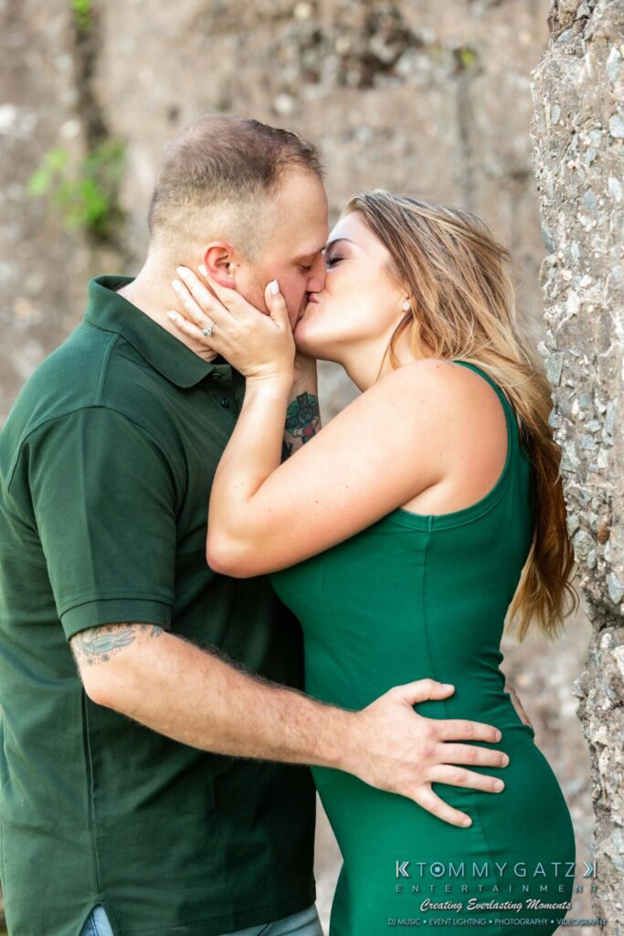063019-Melanie-Rob-FINALS-Low-Res-WM-5 - TOMMY GATZ ENTERTAINMENT A couple in matching green outfits shares a kiss against a rocky background.