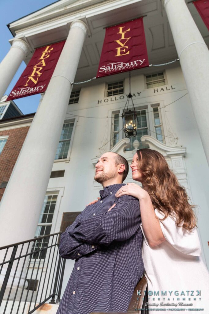 A couple stands in front of Holloway Hall at Salisbury University, looking upwards, with Library banners visible above.