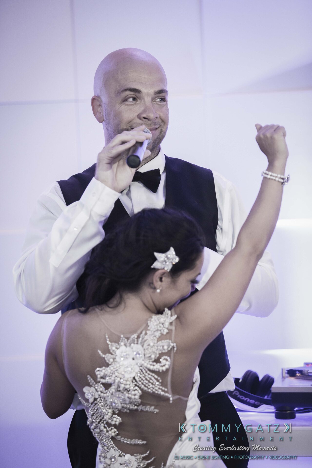 134 - TOMMY GATZ ENTERTAINMENT A man in formal wear holds a microphone, while a woman in a detailed dress, facing away, raises her arm in celebration.