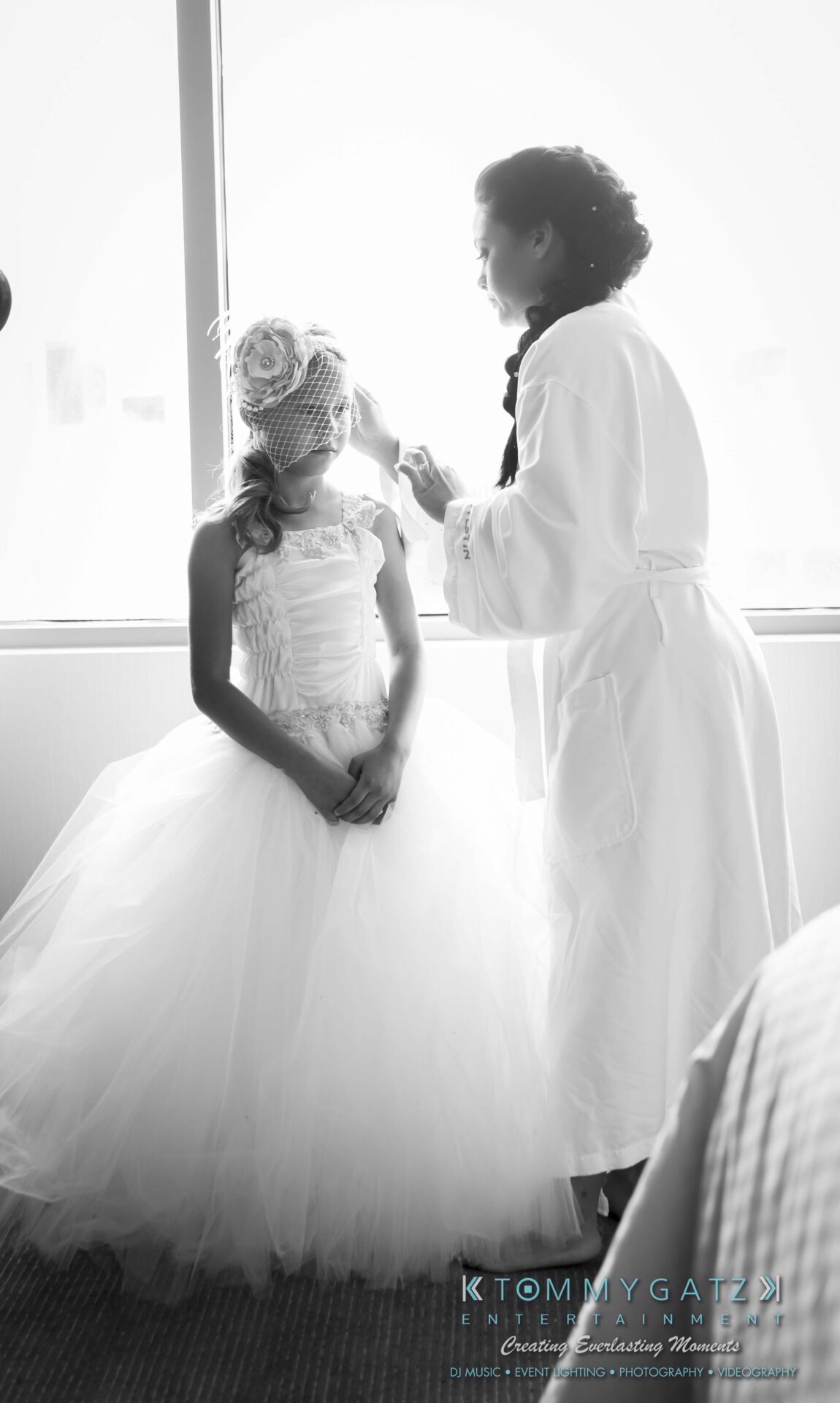 201 - TOMMY GATZ ENTERTAINMENT A woman in a robe adjusts a young girl's headpiece. The girl is wearing a white dress with a tulle skirt.