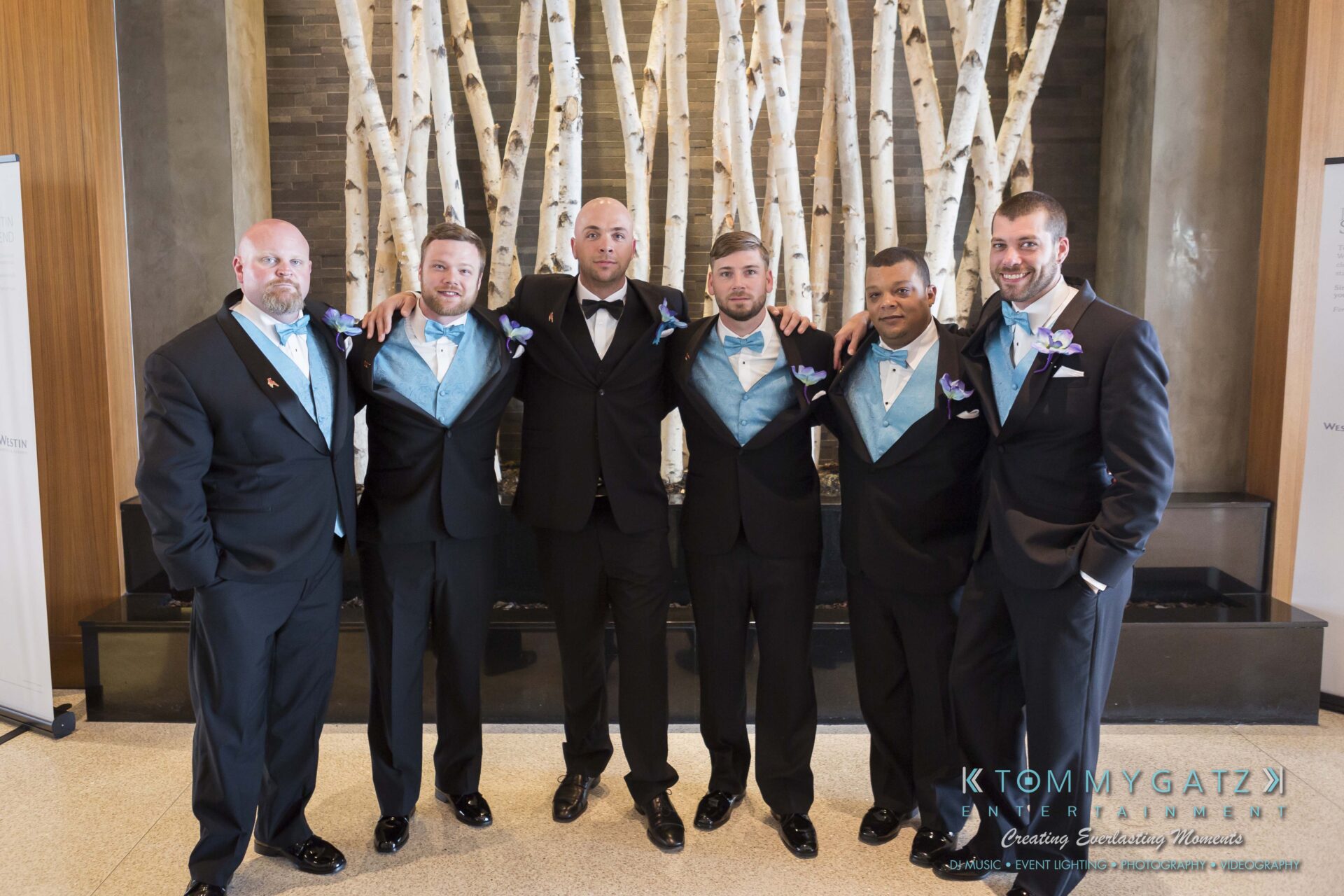 311 - TOMMY GATZ ENTERTAINMENT A group of six men in formal attire pose together indoors in front of a birch tree backdrop.