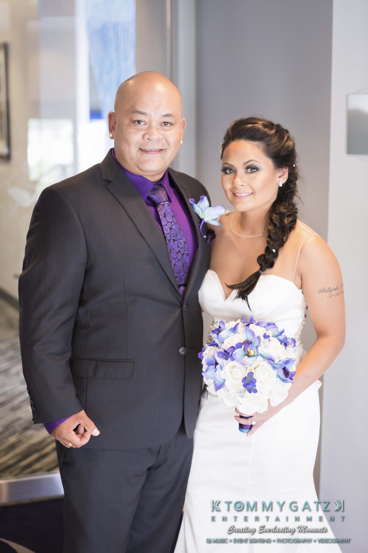 341 - TOMMY GATZ ENTERTAINMENT A man in a suit and a woman in a bridal gown holding a bouquet, posing together indoors.