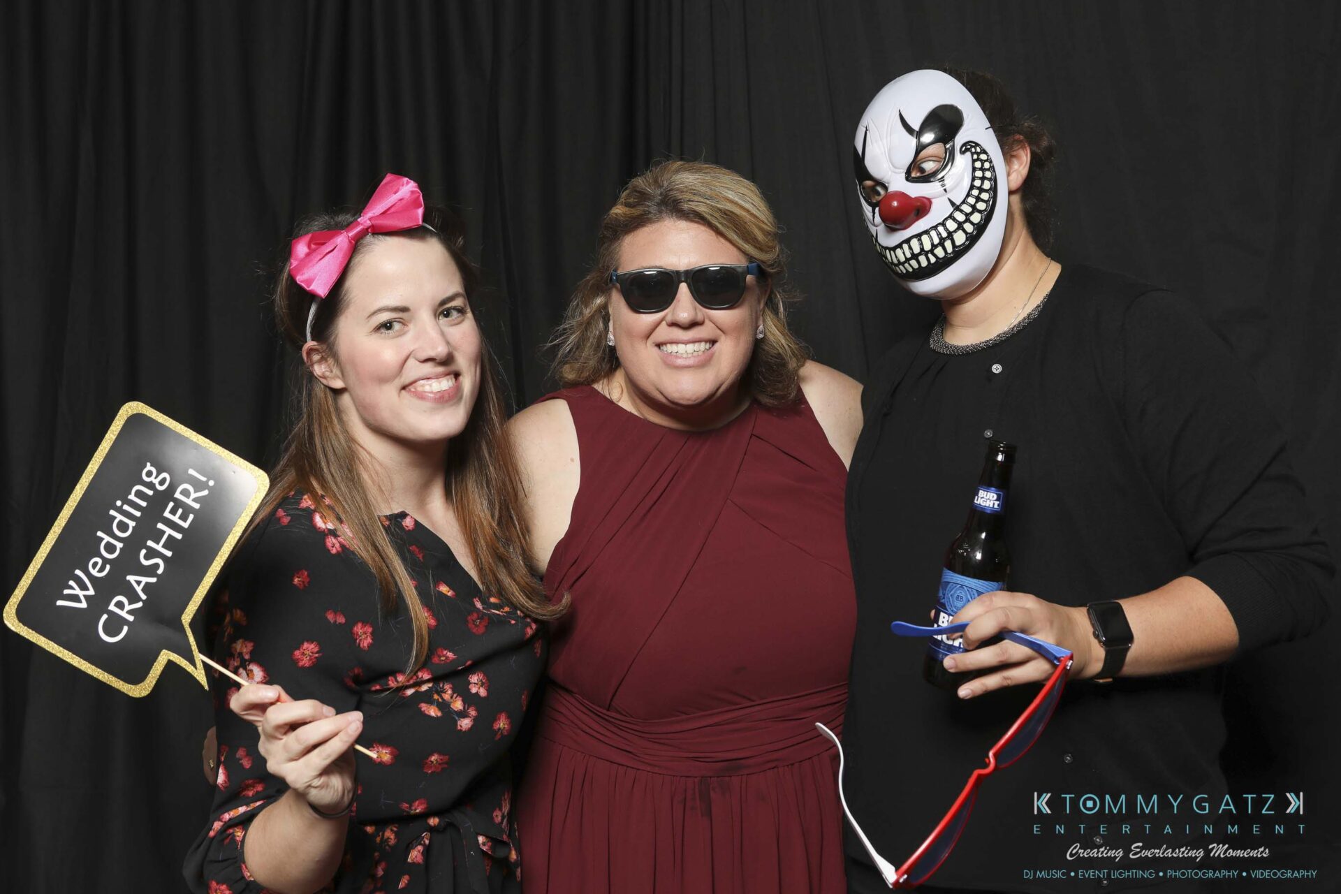 Megan-Matt-102718-Blow-WM-10 - TOMMY GATZ ENTERTAINMENT Three people posing in a photo booth; one holds a "Wedding Crasher" sign, another wears a clown mask, and the third wears sunglasses.