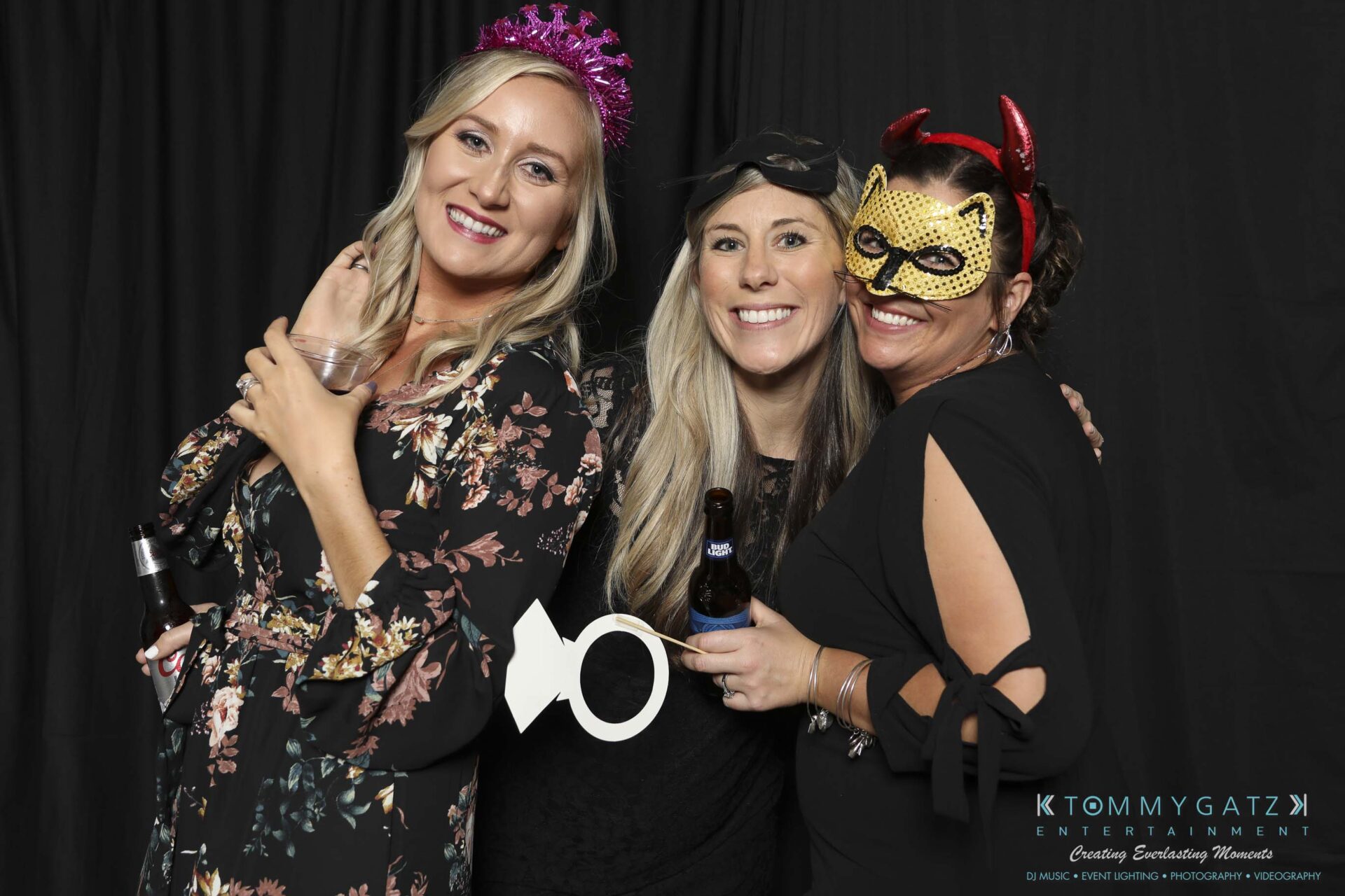 Megan-Matt-102718-Blow-WM-20 - TOMMY GATZ ENTERTAINMENT Three women pose together at a party. One holds a key prop, another wears a mask with devil horns, and the third wears a tiara. They are smiling against a dark backdrop.