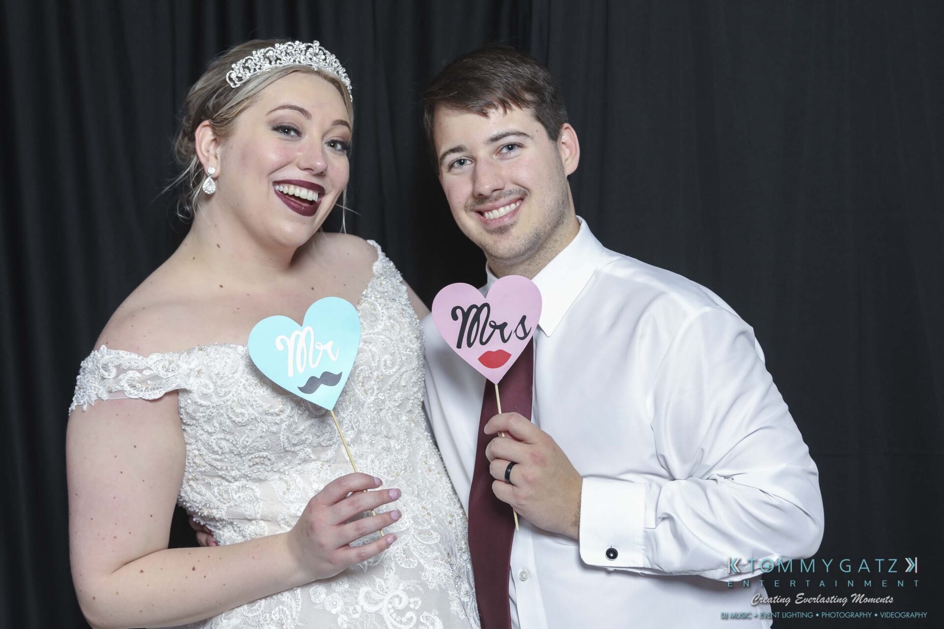 Megan-Matt-102718-Blow-WM-31 - TOMMY GATZ ENTERTAINMENT A bride and groom pose together, each holding a heart-shaped sign. The bride's sign says "Mrs" with lips, and the groom's sign says "Mr" with a mustache. They are smiling at the camera.