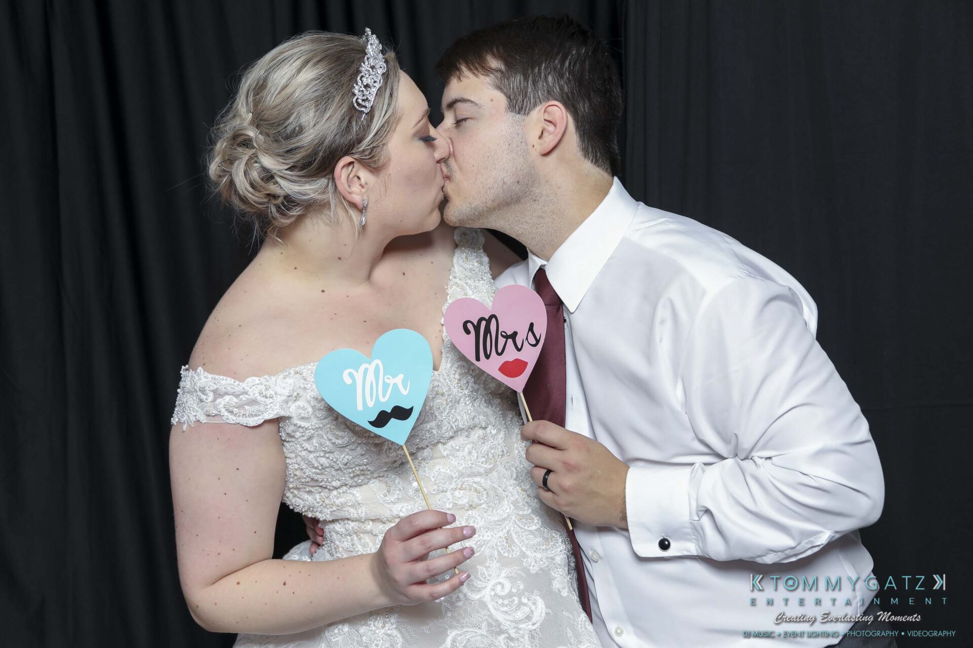 Megan-Matt-102718-Blow-WM-32 - TOMMY GATZ ENTERTAINMENT A couple in formal attire kisses while holding heart-shaped signs with "Mr." and "Mrs." written on them.