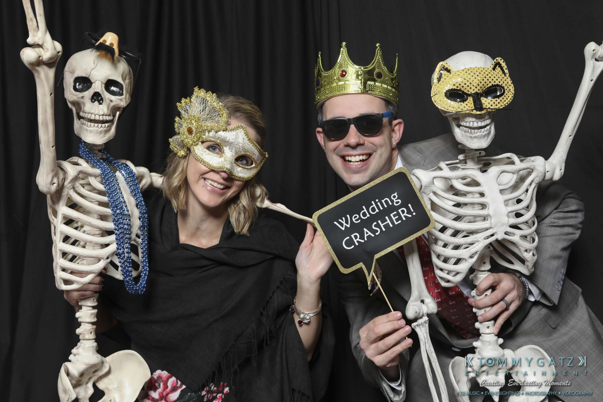 Megan-Matt-102718-Blow-WM-4 - TOMMY GATZ ENTERTAINMENT Two people pose with skeletons dressed in crowns and masks. One holds a "Wedding Crasher!" sign.