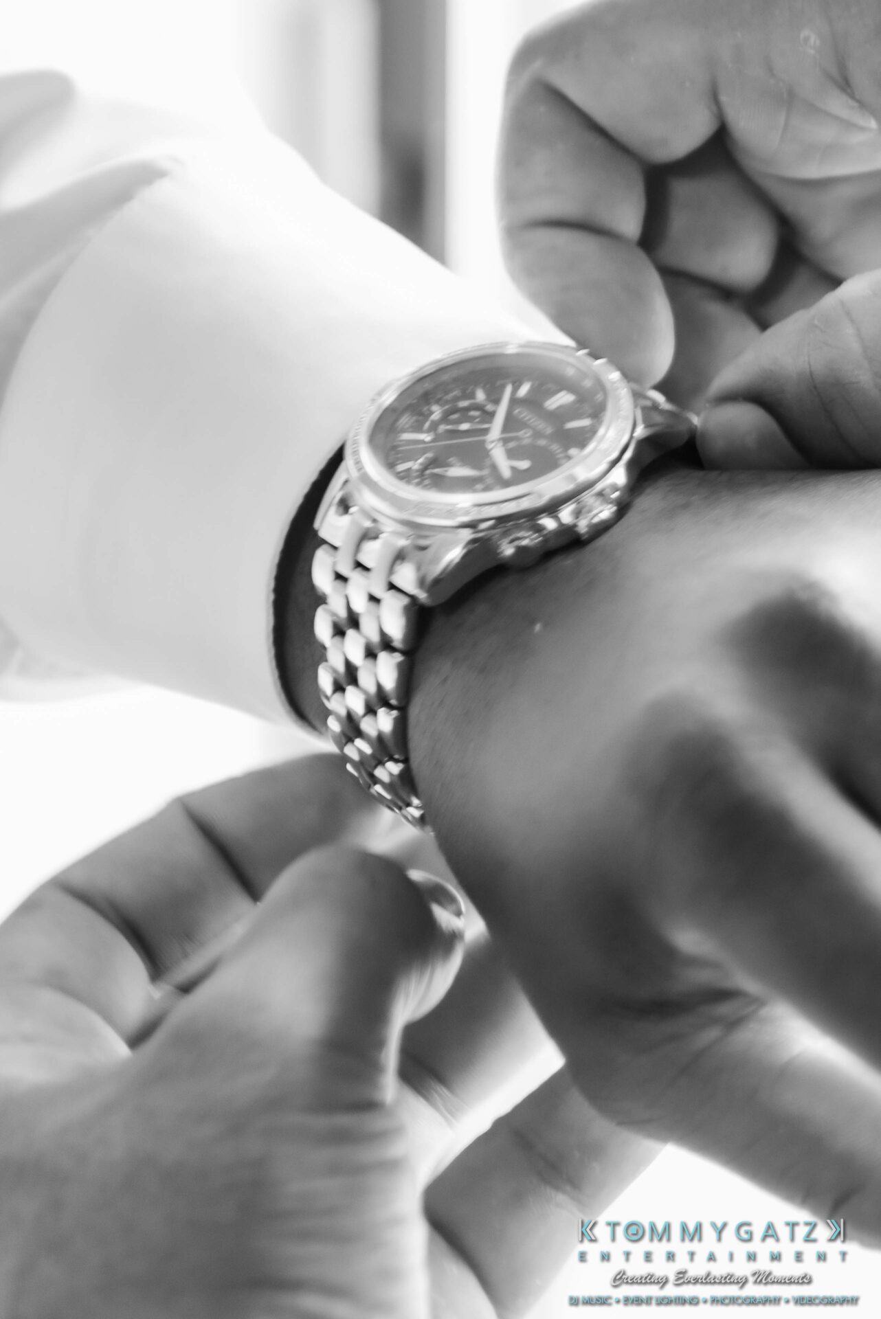 090119-Harris-Wedding-FINALS-Pre-Ceremony-Low-Res-WM-176 - TOMMY GATZ ENTERTAINMENT Close-up of a person fastening a silver watch on their wrist. The watch has a circular face and a metal band.