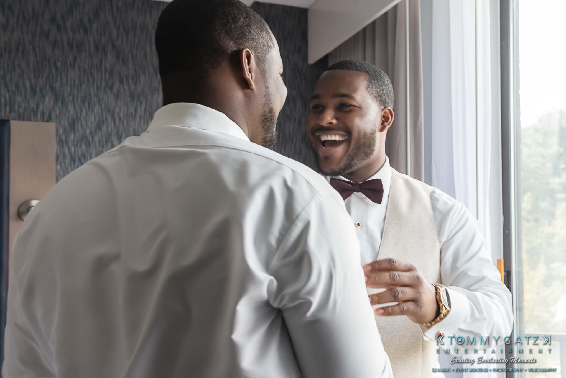 090119-Harris-Wedding-FINALS-Pre-Ceremony-Low-Res-WM-177 - TOMMY GATZ ENTERTAINMENT Two men in white shirts and vests face each other, smiling. They appear to be in a room with a window and grey walls.
