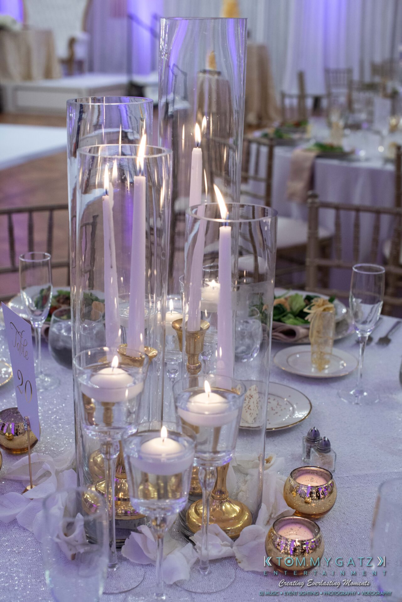 090119-Harris-Wedding-FINALS-Reception-Low-Res-WM-457 - TOMMY GATZ ENTERTAINMENT Tall glass vases with white candles on a decorated table, surrounded by small votives and purple lighting.