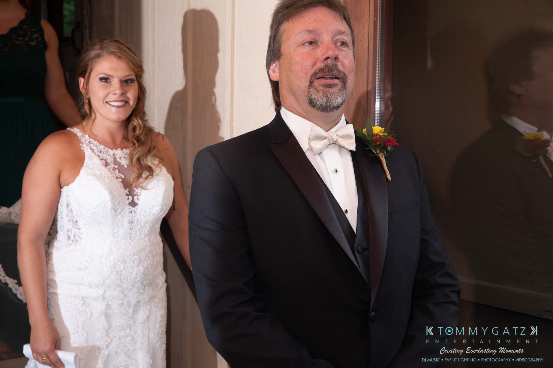 091419-Proctor-Wedding-FINALS-PreCeremony-Low-Res-WM-144 - TOMMY GATZ ENTERTAINMENT A bride in a white gown stands smiling behind a groom in a tuxedo, ready for a first-look moment indoors.