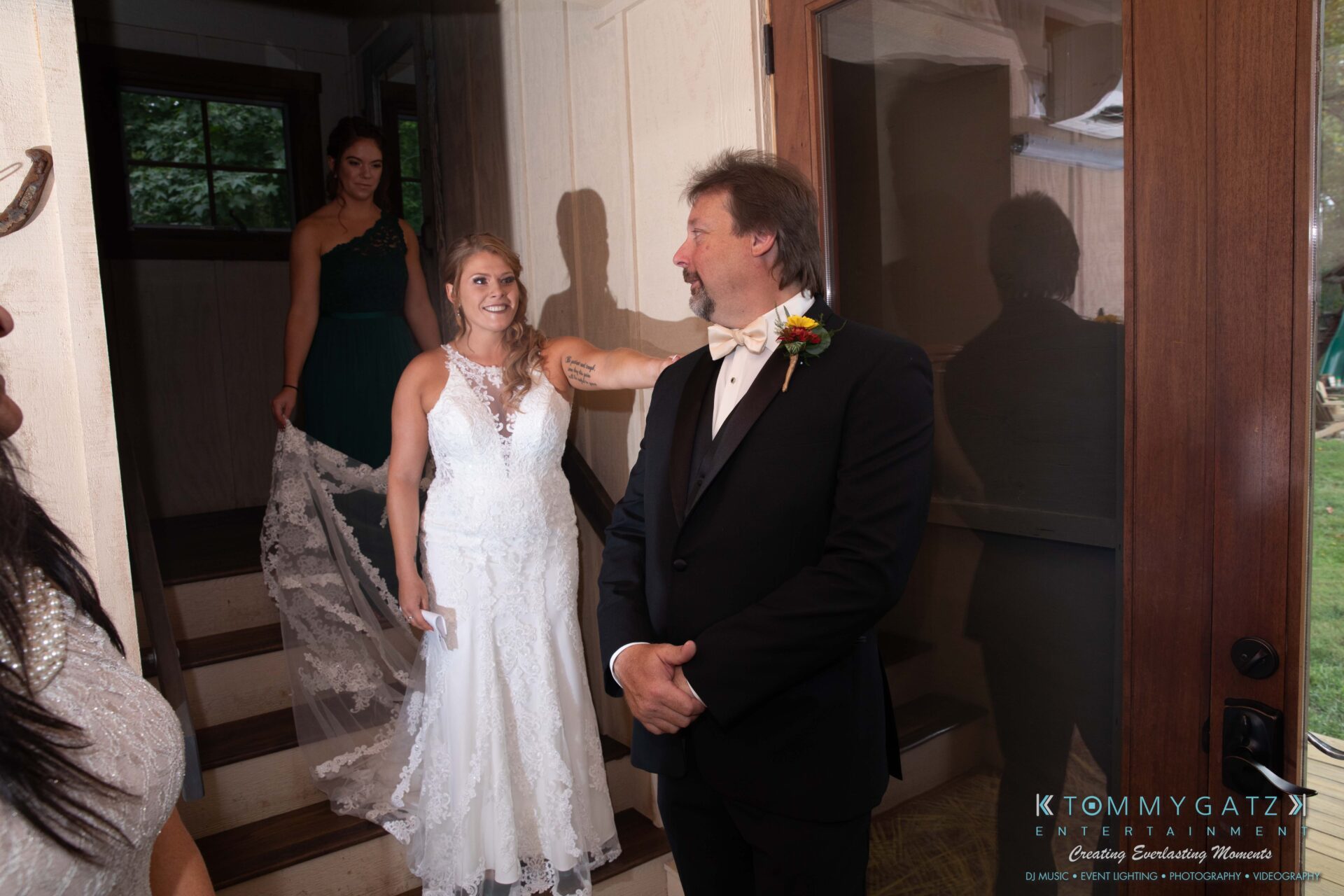 091419-Proctor-Wedding-FINALS-PreCeremony-Low-Res-WM-145 - TOMMY GATZ ENTERTAINMENT Bride in a white dress smiles as she approaches a man in a suit. Another woman holds the train of the bride's dress.