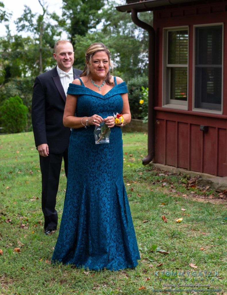 091419-Proctor-Wedding-FINALS-PreCeremony-Low-Res-WM-99 - TOMMY GATZ ENTERTAINMENT A woman in a blue dress stands in front of a man in a suit outdoors near a building.