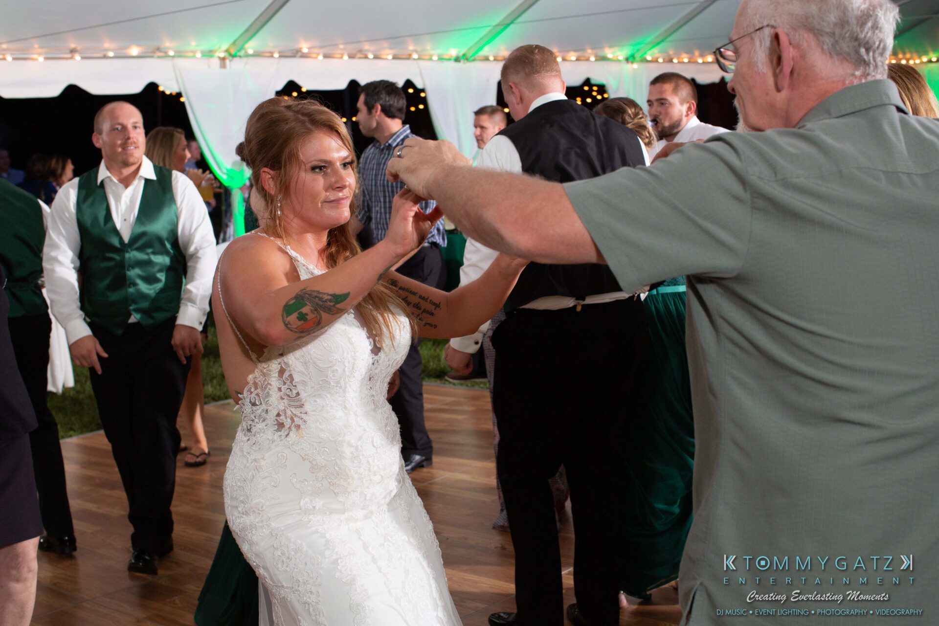 091419-Proctor-Wedding-FINALS-Reception-Low-Res-WM-736 - TOMMY GATZ ENTERTAINMENT A bride in a white dress dances with an older man under a tent. Guests in formal attire stand and watch.