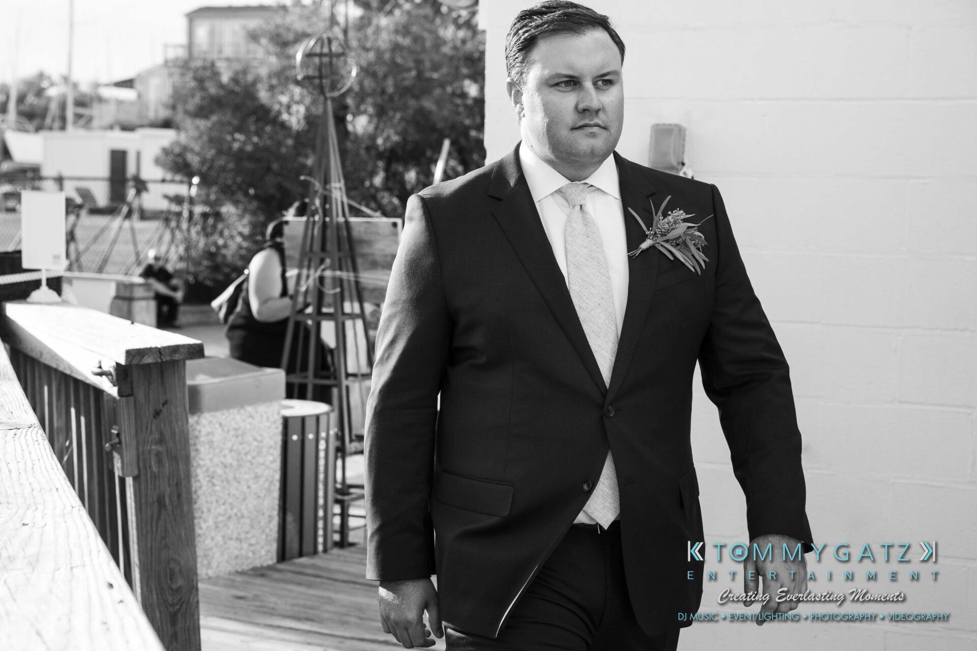 A man in a suit with a boutonniere walks along a wooden deck.