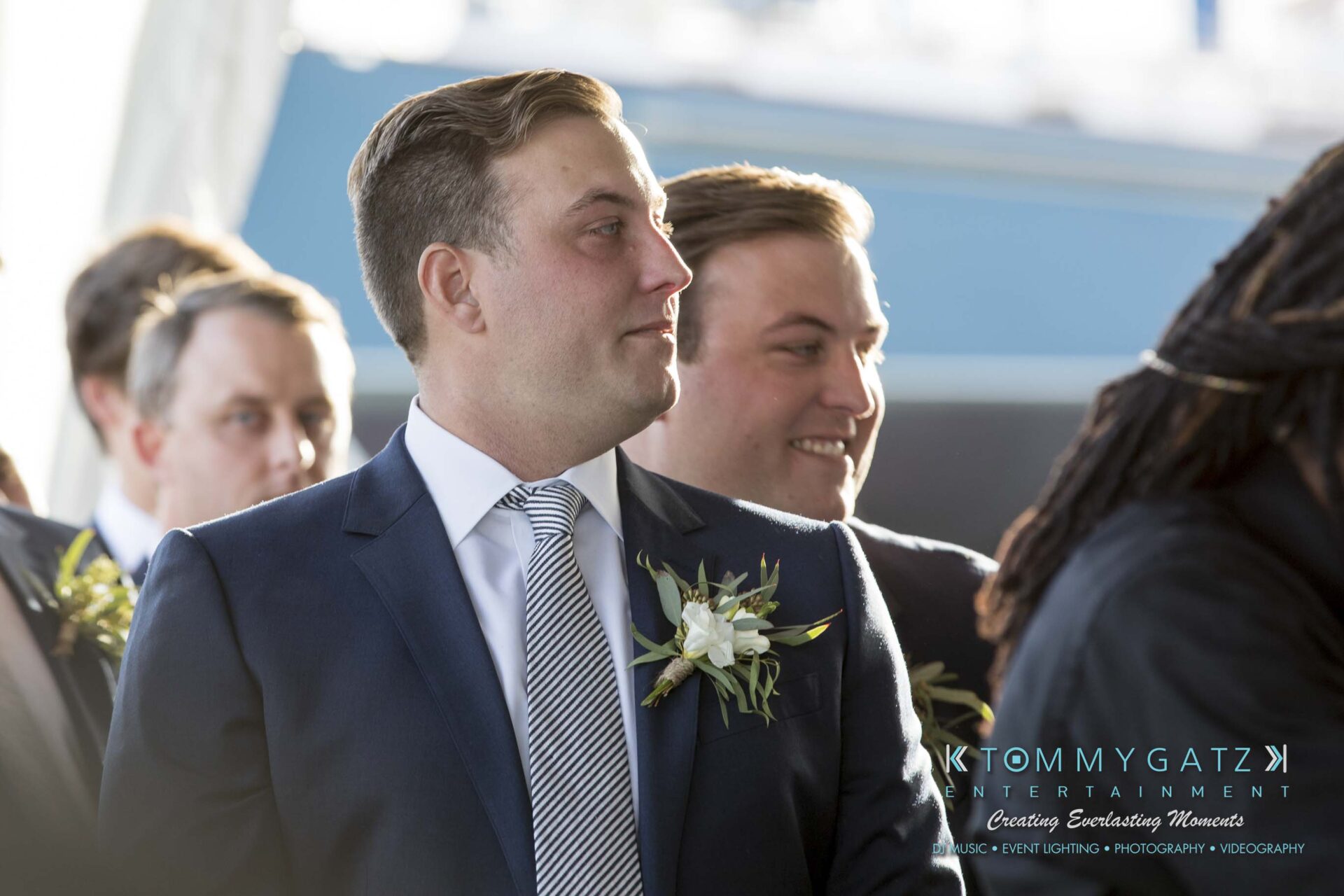 A group of men in suits, some wearing boutonnieres, stand together at an event.