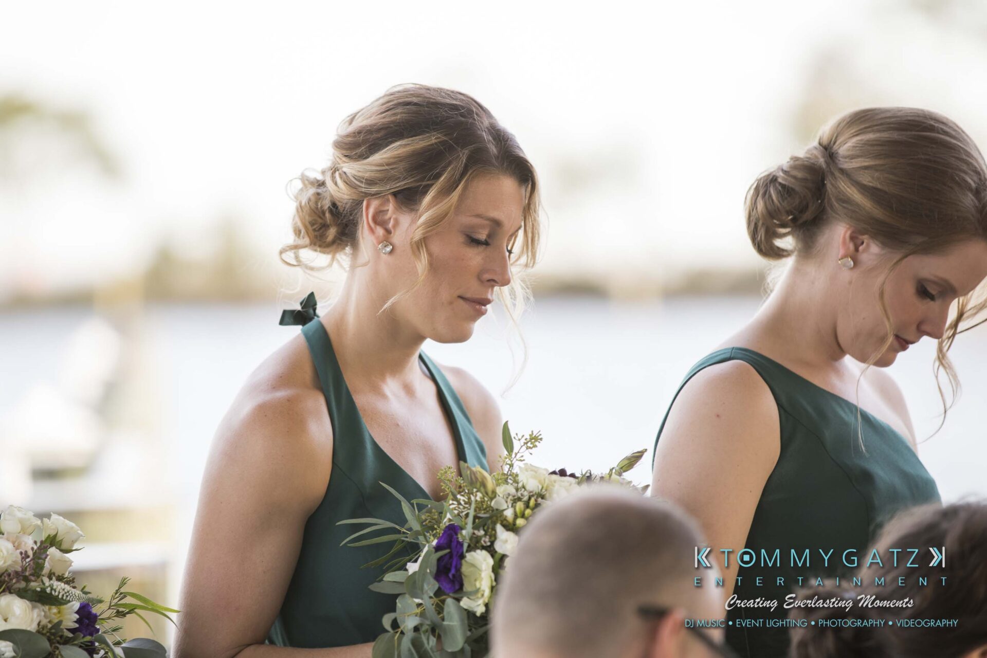 Amanda-Tyler-102117-CEREMONY-Low-Res-WM-47 - TOMMY GATZ ENTERTAINMENT Two women in green dresses hold flower bouquets at an outdoor event by the water.