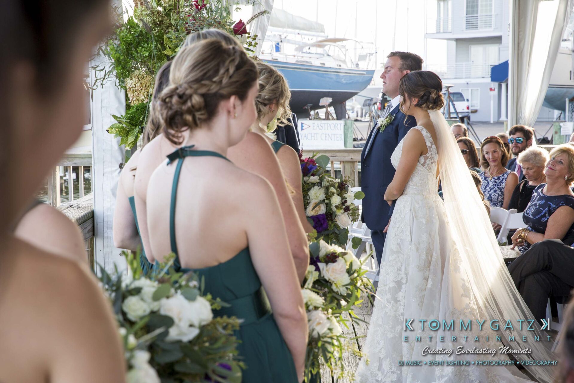 Amanda-Tyler-102117-CEREMONY-Low-Res-WM-57 - TOMMY GATZ ENTERTAINMENT A bride and groom stand at the altar during an outdoor wedding ceremony, surrounded by bridesmaids in green dresses and guests seated nearby.
