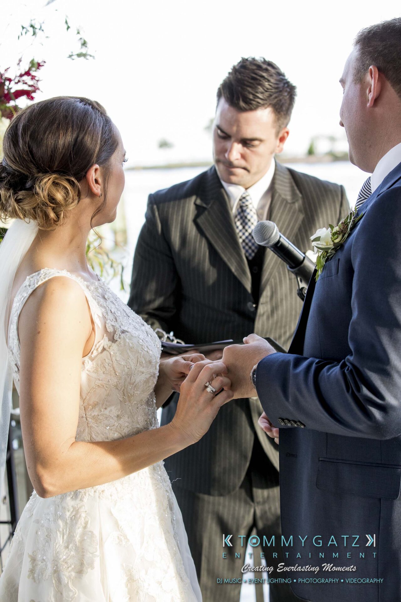 Amanda-Tyler-102117-CEREMONY-Low-Res-WM-73 - TOMMY GATZ ENTERTAINMENT A bride and groom exchange rings during a wedding ceremony, with a man holding a microphone officiating.