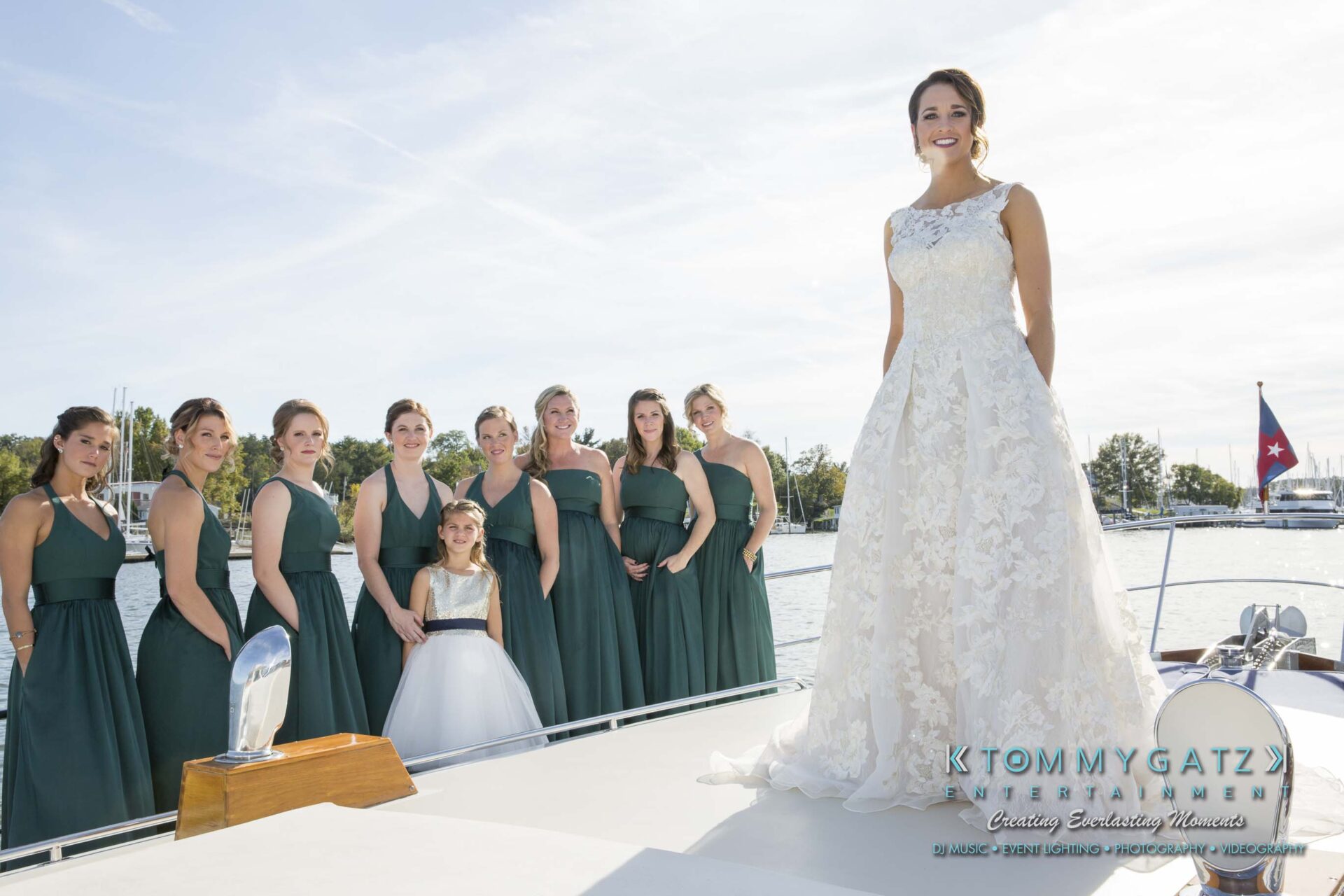 Amanda-Tyler-102117-PREP-Low-Res-WM-109 - TOMMY GATZ ENTERTAINMENT Bride in a white gown stands on a boat with seven bridesmaids in green dresses and a flower girl. Background features a sunny sky and water.