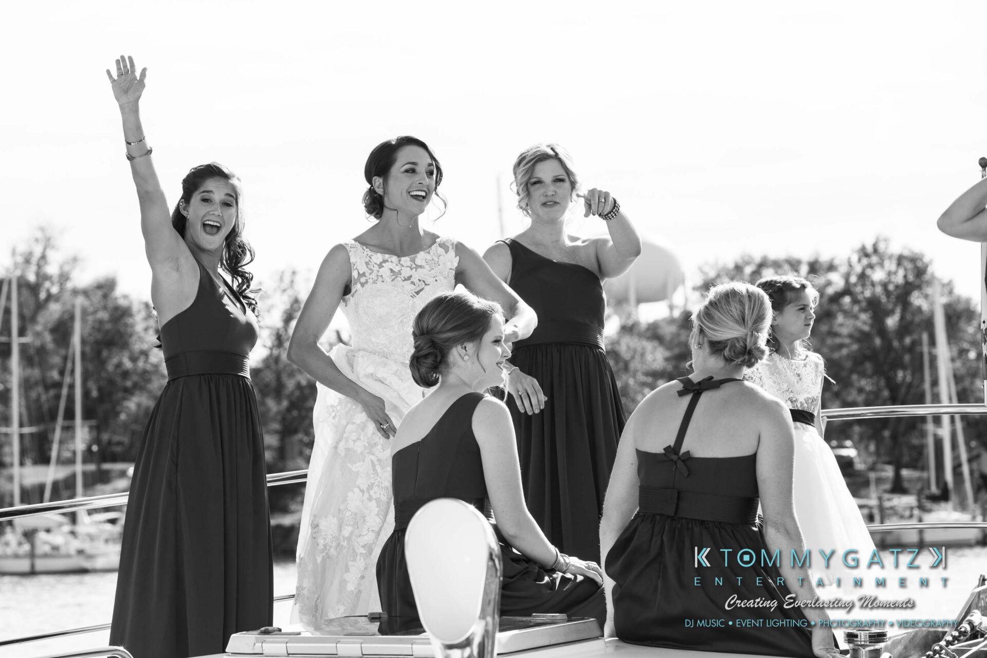 Amanda-Tyler-102117-PREP-Low-Res-WM-142 - TOMMY GATZ ENTERTAINMENT A group of women in formal dresses are standing on a boat. The woman on the left has her arm raised. Trees and a marina are visible in the background.