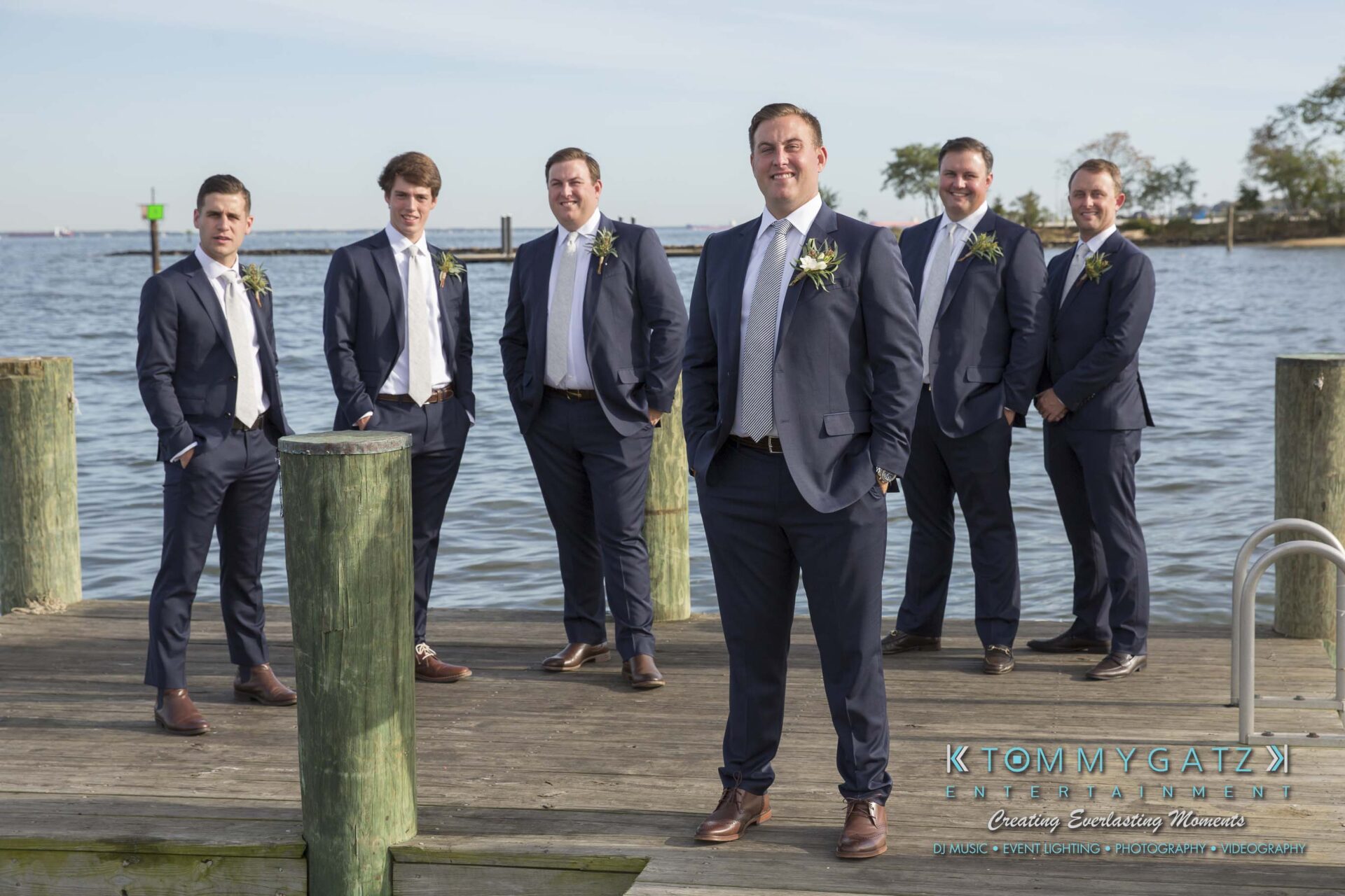 Amanda-Tyler-102117-PREP-Low-Res-WM-167 - TOMMY GATZ ENTERTAINMENT Six men in suits stand on a wooden dock near a waterfront, some with hands in pockets.