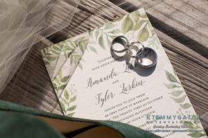 Wedding invitation on a textured paper with green leafy design, featuring two silver rings placed on top.