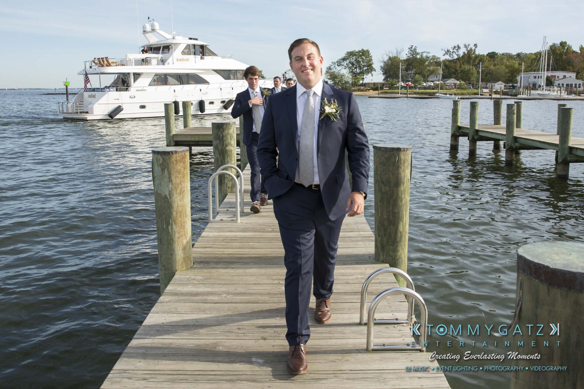 Amanda-Tyler-102117-PREP-Low-Res-WM-170 - TOMMY GATZ ENTERTAINMENT A man in a suit walks along a wooden pier with a yacht in the background on a sunny day.