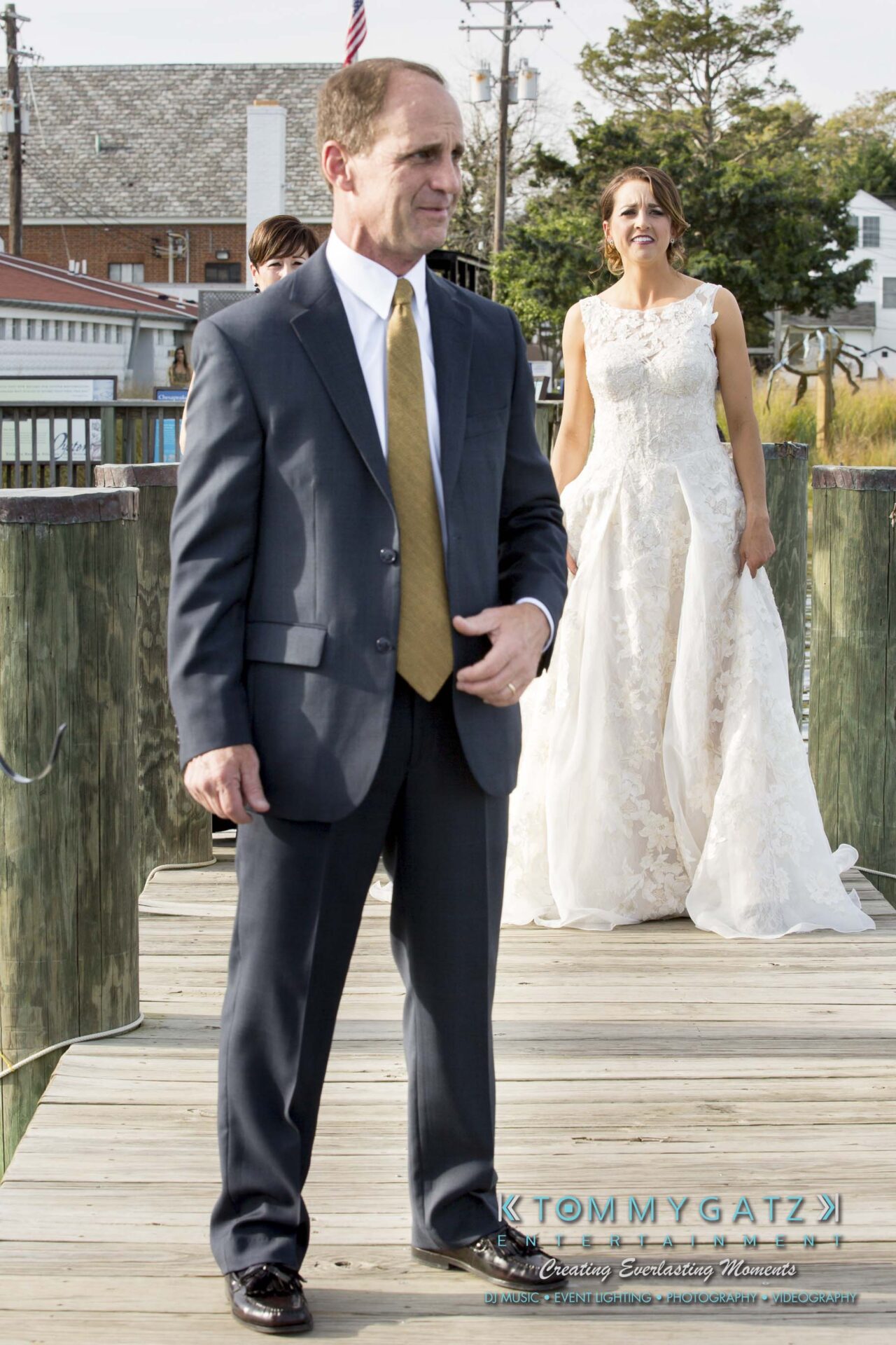 Amanda-Tyler-102117-PREP-Low-Res-WM-179 - TOMMY GATZ ENTERTAINMENT A man in a suit stands on a pier while a woman in a bridal gown smiles in the background.